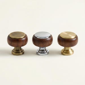 May include: Three cabinet knobs with a dark wood base and a metal top. The knobs have a mushroom shape, with the metal tops in brass and chrome finishes. The knobs are designed for furniture and home decor.
