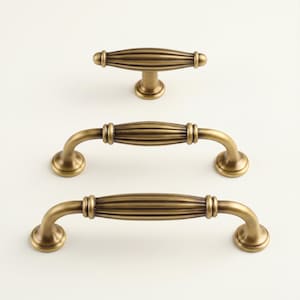 May include: Three antique brass cabinet hardware pieces. The set includes a knob and two different sized pulls. Each piece has a ribbed center design and rounded ends. The hardware is displayed on a white background.