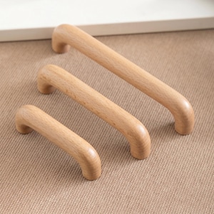 Peut inclure: Trois poignées de meubles en bois de différentes tailles. Les poignées sont en bois clair et ont un design incurvé et arqué. Les poignées sont disposées en diagonale, mettant en valeur leurs différentes longueurs.