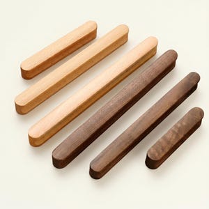 May include: A selection of wooden cabinet pulls in shades of brown. The pulls are rectangular with rounded ends, displaying the natural wood grain. The pulls are arranged diagonally, showing the different wood tones. The lengths vary.