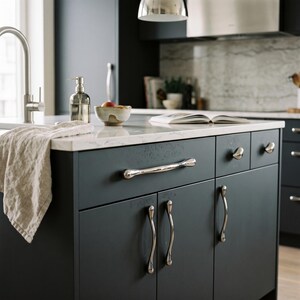 Puede incluir: Isla de cocina moderna con gabinetes azul oscuro y encimera de m&aacute;rmol blanco. Tiradores y pomos plateados pulidos adornan las puertas y cajones de los gabinetes. Un cuenco de fruta, un dispensador de jab&oacute;n y una toalla de lino est&aacute;n en la encimera.