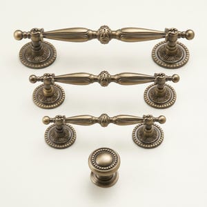 May include: A collection of antique bronze cabinet hardware, featuring three pull handles and a knob. The handles have an ornate design with decorative circular backplates. The knob is round with a beaded edge. Suitable for kitchen or bathroom cabinets.