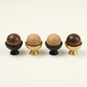 May include: Four decorative wooden spheres, two dark brown and two light brown, sit atop small, pedestal-style holders. The holders alternate between black and gold-colored metal, creating a contrasting visual appeal. The spheres appear to be made of wood.
