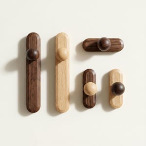 May include: A collection of wooden wall hooks in various shapes and wood tones. The hooks feature a rounded knob at the end of a rectangular or oval base. The wood colors range from light to dark brown.