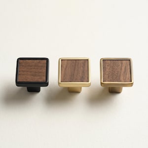 May include: Three square cabinet knobs with wood grain centers. One knob has a black base and frame, while the other two have gold-toned bases and frames. The knobs are designed for furniture and home decor.
