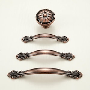May include: A set of antique-style cabinet hardware in a bronze finish. The set includes a round knob with a floral design and three matching pull handles. The hardware is designed for use on drawers and cabinets.