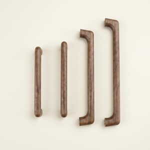 May include: Four wooden cabinet pulls in varying sizes. The pulls are a warm brown color and have a smooth, curved design. The two larger pulls have a distinctive angled shape at the ends, while the smaller ones are straight. These are ideal for kitchen or bathroom cabinets.
