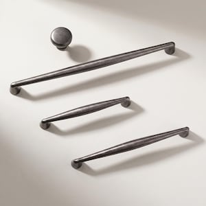 May include: A set of four antique-style cabinet hardware pieces in a dark, weathered metal finish. The set includes a round knob and three different-sized bar pulls, ranging from approximately 5 to 12 inches in length, all with a tapered design.