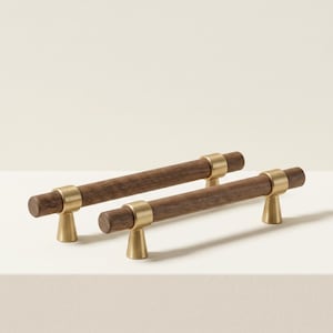 May include: Two wooden cabinet pulls with a dark brown finish and brass-colored accents. The pulls have a cylindrical shape with a brass ring in the center and are mounted on brass-colored, cone-shaped feet. These decorative pulls are ideal for kitchen or bathroom cabinets.