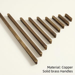 May include: A collection of solid brass handles in varying lengths, arranged diagonally on a white surface. The handles have a warm, copper-toned finish. Text at the bottom reads "Material: Copper Solid brass Handles."