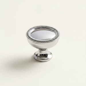Peut inclure: Bouton de meuble argenté poli, avec un bord rond perlé et une surface lisse et réfléchissante. Monté sur une base courte en forme de piédestal. Convient aux tiroirs et aux armoires. Design classique et élégant.