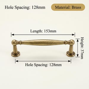 May include: Brass cabinet pull with a vintage finish. The pull is 15.3cm long, with a height of 3.7cm and a hole spacing of 12.8cm. The material is brass.