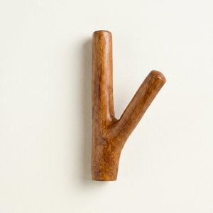 May include: A wooden wall hook in the shape of a tree branch. The hook is a warm brown color and has a smooth finish. The branch extends at a 45-degree angle from the main stem. This decorative hook is ideal for hanging coats, hats, or other items.