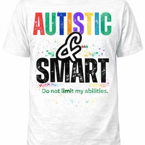 Pode incluir: Camiseta branca com as palavras "AUTISTIC & SMART" em texto colorido e desgastado. A camiseta também inclui a frase "Do not limit my abilities" em uma fonte menor, com respingos de tinta coloridos.