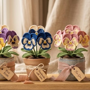 Peut inclure: Quatre arrangements de fleurs de pensées faites à la main au crochet dans de petits pots. Les pensées sont dans des tons de violet, de bleu, de rose et de jaune. Chaque pot est décoré d'un ruban et d'une étiquette avec "For Mom", "Handmade with Love" ou "For You".
