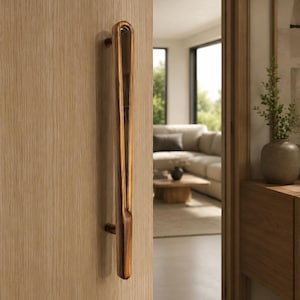 Puede incluir: Un tirador de puerta vertical con un acabado de grano de madera oscura pulida y una forma de gota alargada y suave. El tirador está montado en una puerta de madera clara con grano vertical, mostrando un diseño curvo con un centro reflectante.