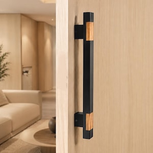 May include: A vertical door handle featuring a long, matte black rectangular bar accented with two light-toned wood inserts near the top and bottom mounting points, securely attached to a light-colored wooden door surface.