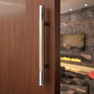 May include: A vertical door handle mounted on a wooden door. The handle features a long, cylindrical, matte champagne-colored center section with tiered, polished chrome-finished accents at both the top and bottom ends of the hardware.