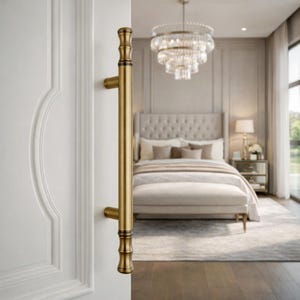 May include: A vertical, cylindrical door handle with a brushed brass finish, featuring decorative grooved detailing at the top and bottom ends. The handle is mounted onto a white door panel with a raised, curved molding design.