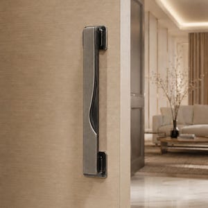 Pode incluir: Um puxador de porta retangular vertical com acabamento metálico escovado e uma ranhura central escura e rebaixada. O puxador está montado numa porta de cor clara com textura de madeira, apresentando um design elegante e alongado com dois suportes escuros.