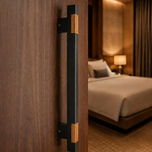 May include: A vertical door handle featuring a long, matte black rectangular bar with two light-toned wooden accents at the top and bottom mounting points, securely attached to a dark brown wooden door with visible grain patterns.