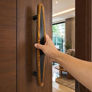 May include: A vertical door handle featuring a long, almond-shaped wooden frame with a smooth, dark matte black centre insert. The handle is mounted onto a dark brown wooden door with two black cylindrical supports at the top and bottom.