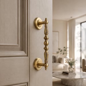 May include: A vertical brass door handle with a decorative spindle design featuring rounded and leaf-like accents, mounted on a light-colored wooden door with two circular base plates that secure the handle to the door surface.