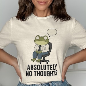 Cream t-shirt with a cartoon frog in a chair, speaking bubble, and "ABSOLUTELY NO THOUGHTS" text.