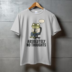 Light gray t-shirt with frog character sitting in chair, text "ABSOLUTELY NO THOUGHTS".