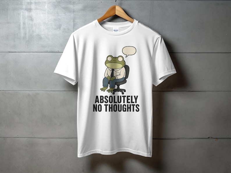 White t-shirt with graphic of a frog wearing a shirt and tie, sitting in a chair, with "ABSOLUTELY NO THOUGHTS" text.