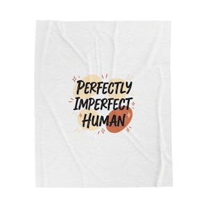 May include: White blanket with the text "Perfectly Imperfect Human" in black, with yellow, orange, and brown accents. The blanket has a soft, textured appearance.
