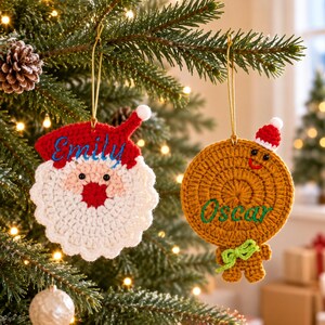 May include: Two crocheted Christmas ornaments hanging from a tree. One is a Santa Claus face with a red hat and the name Emily embroidered in blue. The other is a brown gingerbread person with a small red hat and the name Oscar embroidered in green.