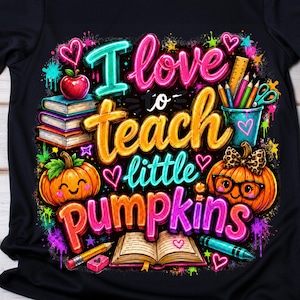 May include: A black short-sleeve t-shirt featuring a colorful graphic with the text "I love to teach little pumpkins." The design includes illustrations of stacked books, a red apple, a pumpkin with glasses, a pencil, and an open book.