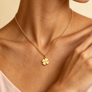Könnte beinhalten: Eine goldfarbene Halskette mit einem vierblättrigen Kleeblatt-Anhänger. Die Halskette wird um den Hals getragen. Der Anhänger ist ein detailliertes Kleeblatt-Design. Die Kette ist ein filigranes, verbundenes Modell.