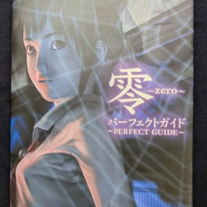 May include: A book titled "The PlayStation2 BOOKS" with the Japanese title "零 ~zero~" and "PERFECT GUIDE" in English and Japanese. The cover features a digitally rendered image of a person with a blue and purple overlay.