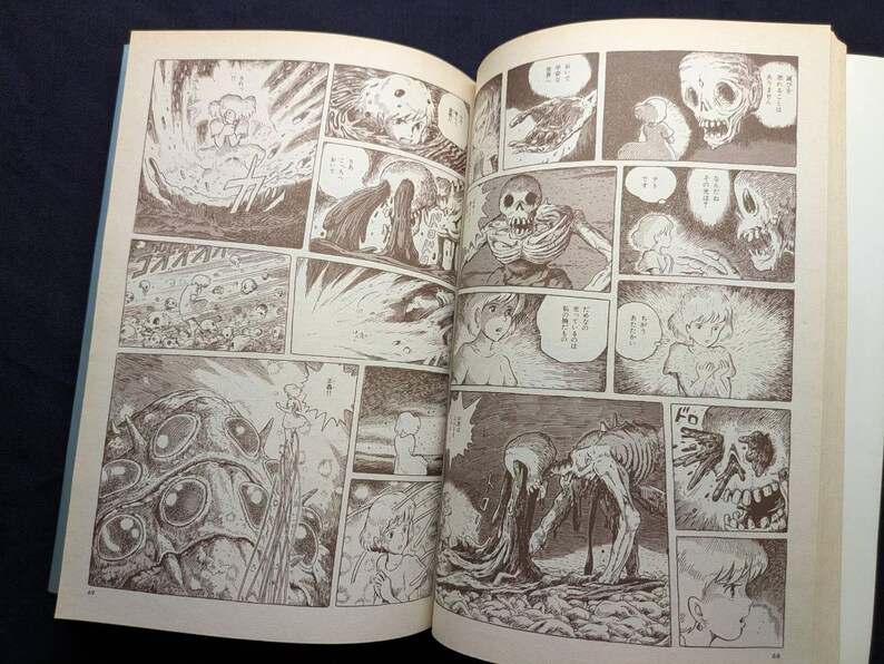 May include: An open book displaying manga panels with detailed illustrations in sepia tones. The panels depict scenes of explosions, skeletal figures, and a young girl. The artwork has a vintage, hand-drawn aesthetic.