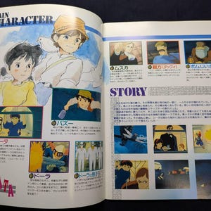 May include: A printed book page featuring illustrations and Japanese text from the film Laputa: Castle in the Sky. The layout includes a Main Character section with character portraits and a Story section with multiple small scene panels.