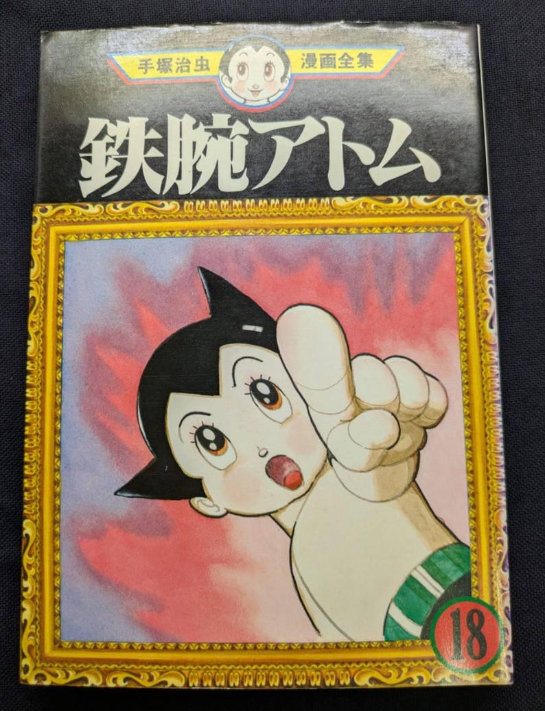 May include: Astro Boy manga volume 18. The cover features a colorful illustration of Astro Boy pointing upwards, framed in gold. The title is in Japanese characters, with additional text at the top.
