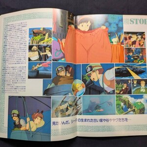 May include: An open book featuring colorful anime-style illustrations from a film story. The pages display multiple scenes, including characters in flight, a person wearing oversized clothing, and text in Japanese. The layout includes the word STORY.