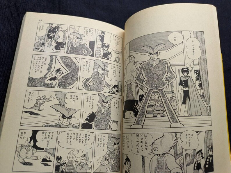 May include: Open book with Japanese manga illustrations. The black and white panels depict various characters in action, with speech bubbles containing Japanese text. The pages are yellowed with age, suggesting a vintage comic book.