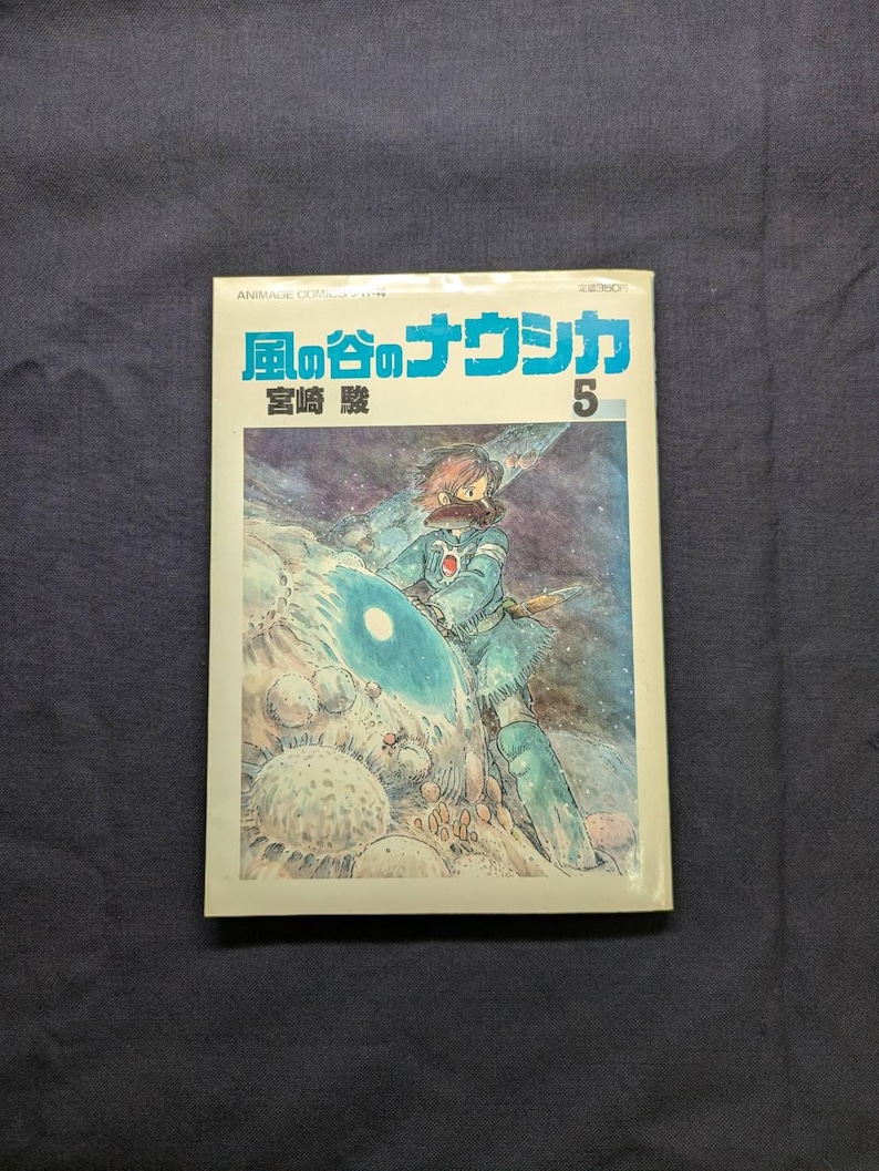 May include: A vintage Japanese manga book titled "Nausica&auml; of the Valley of the Wind" with a vibrant illustration of a character in a blue outfit. The cover features Japanese text and the number 5.