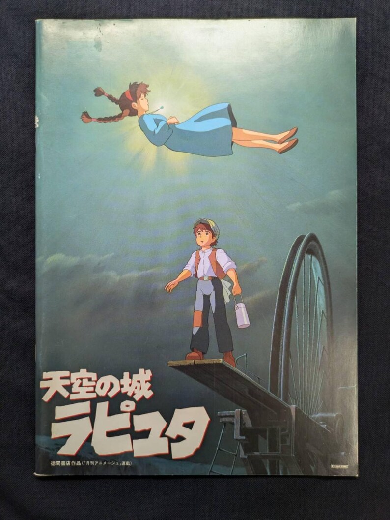 May include: A rectangular poster featuring an animated scene with a person in a blue dress floating in the sky above a person standing on a wooden plank. The text "天空の城ラピュタ" is printed in large white characters at the bottom left corner.
