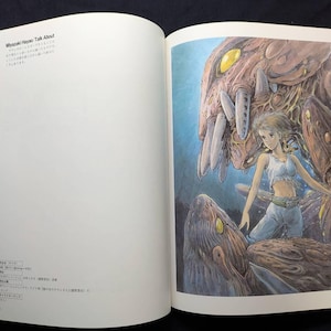 Pu&ograve; includere: Libro aperto con un'illustrazione colorata di una giovane donna con top bianco e pantaloni blu, in piedi vicino a una grande creatura marrone simile a un mostro. L'illustrazione &egrave; in uno stile anime dettagliato. Il testo sulla pagina di sinistra recita "Miyazaki Hayao Talk About".