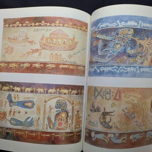 Pu&ograve; includere: Libro aperto che mostra illustrazioni colorate di arte antica. L'opera d'arte presenta barche, figure, animali e simboli in tonalit&agrave; terrose. Le illustrazioni ricordano gli affreschi storici e raffigurano scene con dettagli intricati.