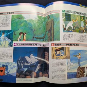 May include: An open book featuring colorful anime-style illustrations from the film Castle in the Sky. The pages display various scenes including a large robot, characters in a forest, a person playing a trumpet, and Japanese text throughout.