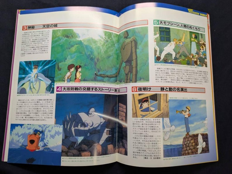 May include: An open book featuring colorful anime-style illustrations from the film Castle in the Sky. The pages display various scenes including a large robot, characters in a forest, a person playing a trumpet, and Japanese text throughout.