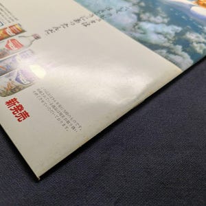 May include: A glossy paper advertisement featuring a blue sky with clouds and a small orange vehicle in the upper right corner. The left side displays four beverage bottles with Japanese text, including the characters 風の味 and 新発売.