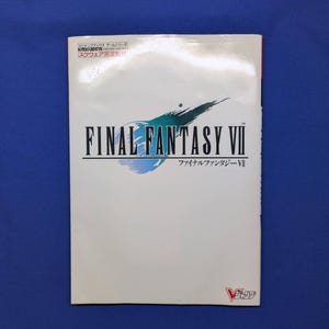 May include: A white softcover book with the Final Fantasy VII logo in black and blue text. The cover features a stylized blue comet graphic, Japanese text in the top left corner, and a red V Jump logo in the bottom right corner.