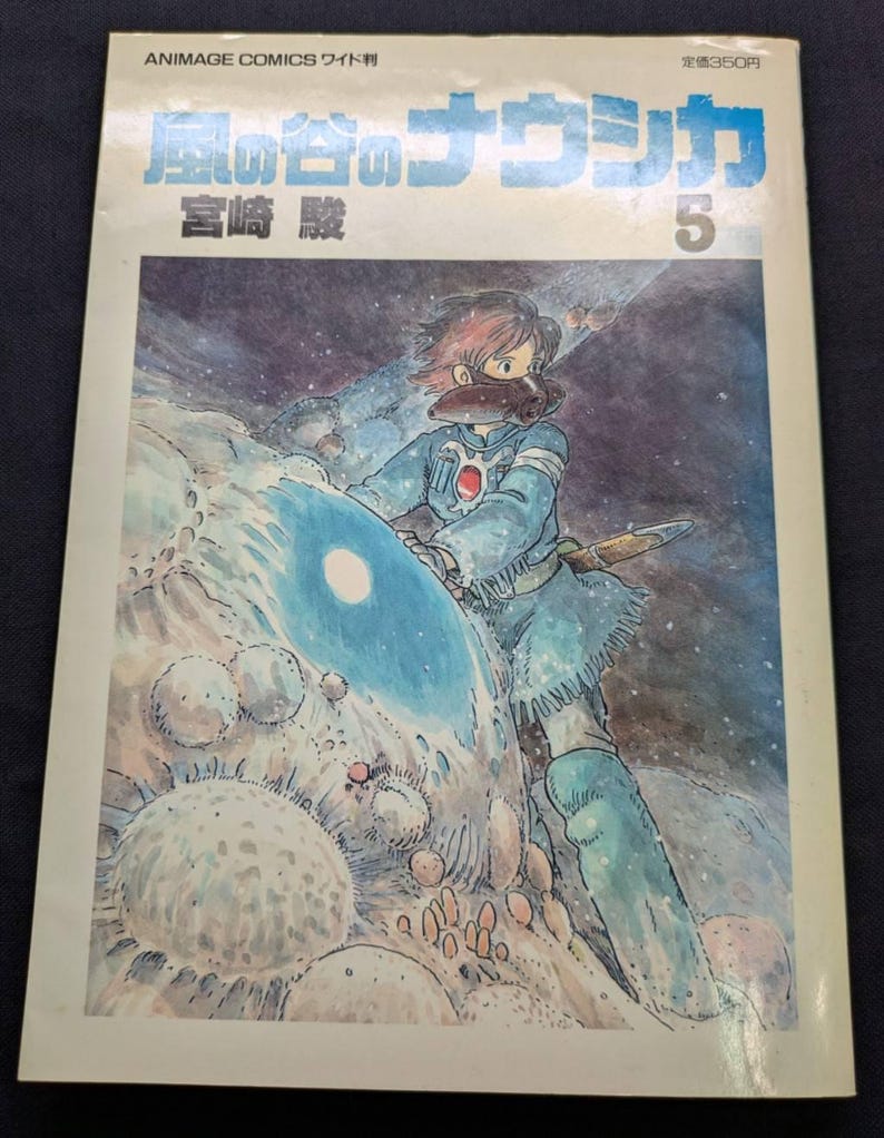 May include: A vintage Japanese manga comic book titled "Nausica&auml; of the Valley of the Wind" with a cover illustration of a character in a blue outfit. The cover features Japanese text and the number 5.