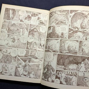 May include: Open book with sepia-toned manga illustrations. The artwork features detailed panels with figures, creatures, and speech bubbles. The style is reminiscent of classic Japanese comics, with a focus on storytelling through sequential art.